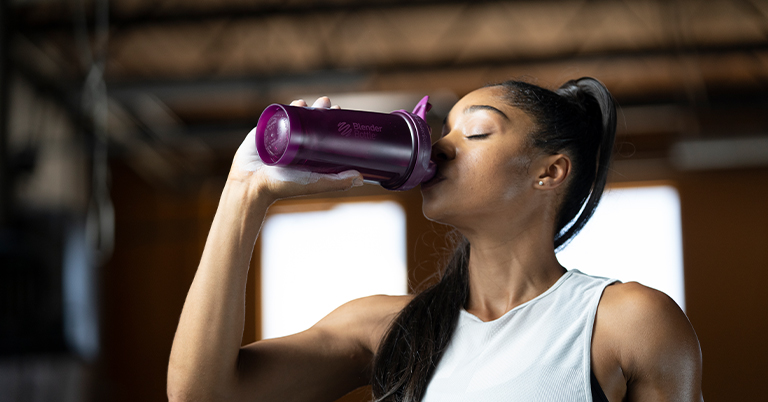 Woman drinking from a BlenderBottle Brand shaker cup. 